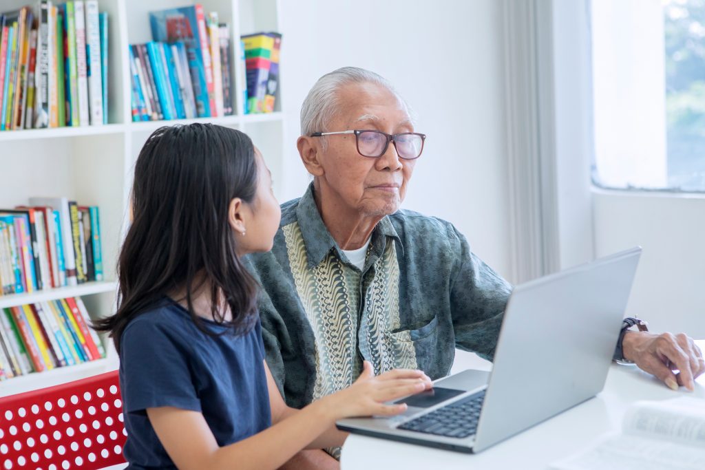 Young girl teaching grandfather how to use the computer