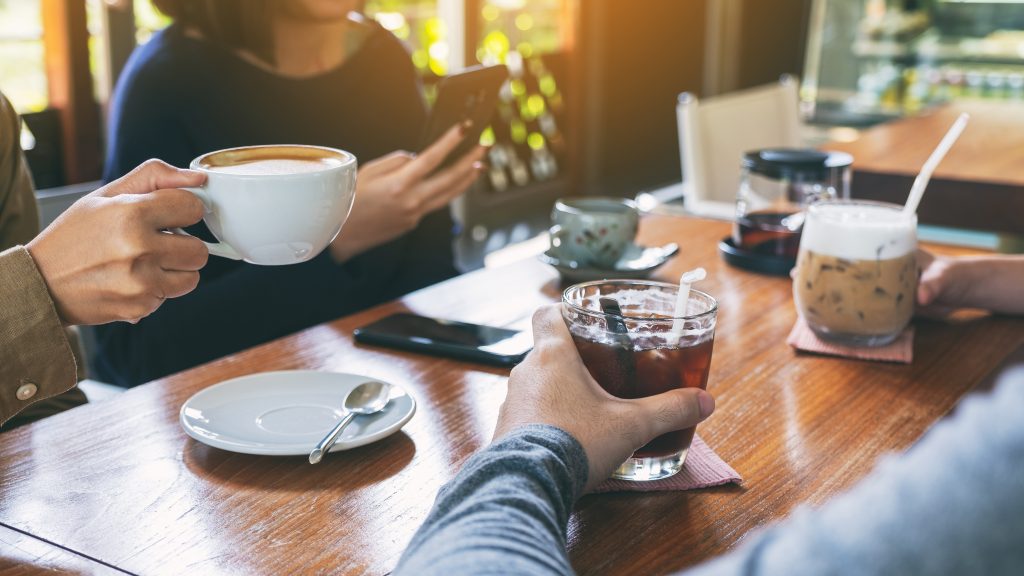 Closeup image of people using mobile phone and drinking coffee together in cafe