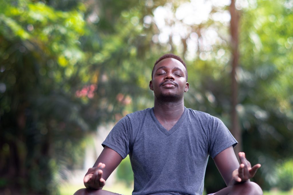 Black man is meditating on green grass in the park