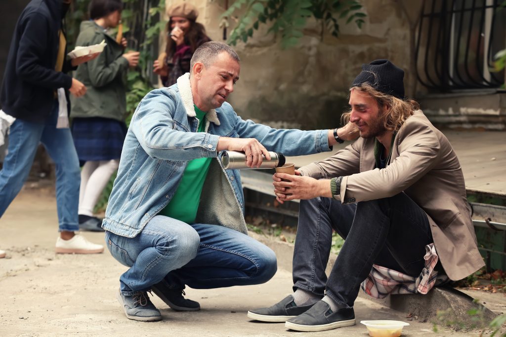 Volunteer giving drink to homeless man outdoors
