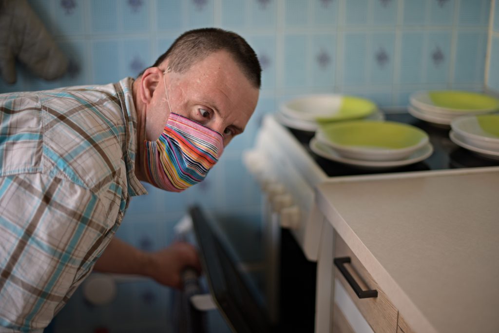 Handicapped young man in a mask opening oven