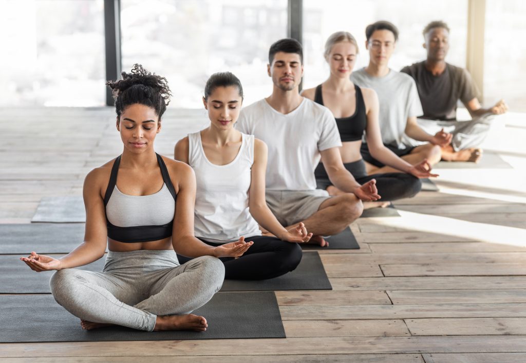 Meditation Class. Group Of Fit Young People Practicing Yoga In Modern Light Studio, 