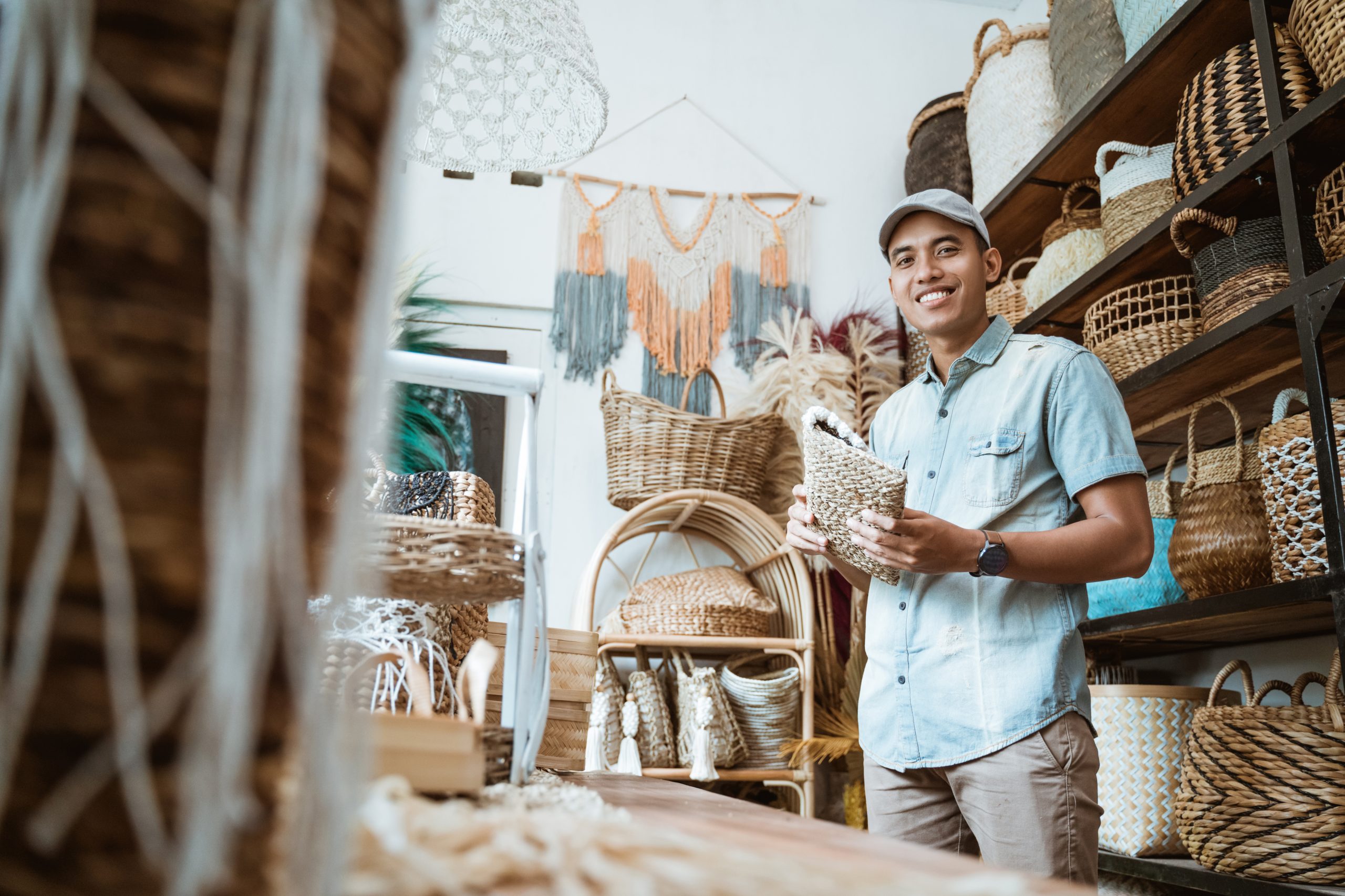young entrepreneur smiles while holding a wicker wallet while standing in a craft shop