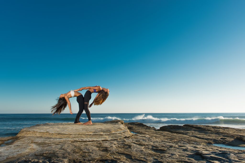 Two women stretching on a rock with waves crashing