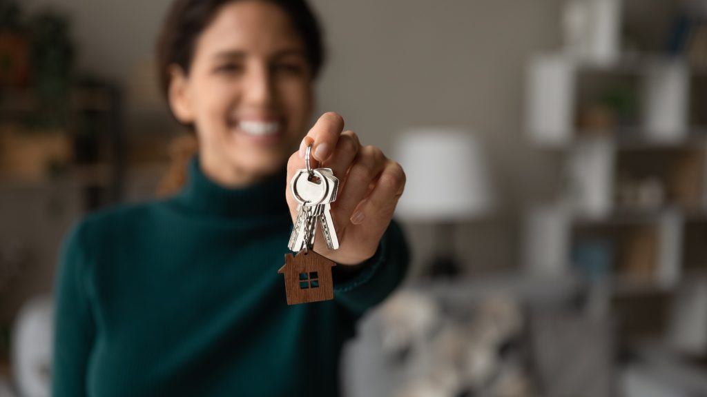 Woman smiling blurred in the background holding out house keys
