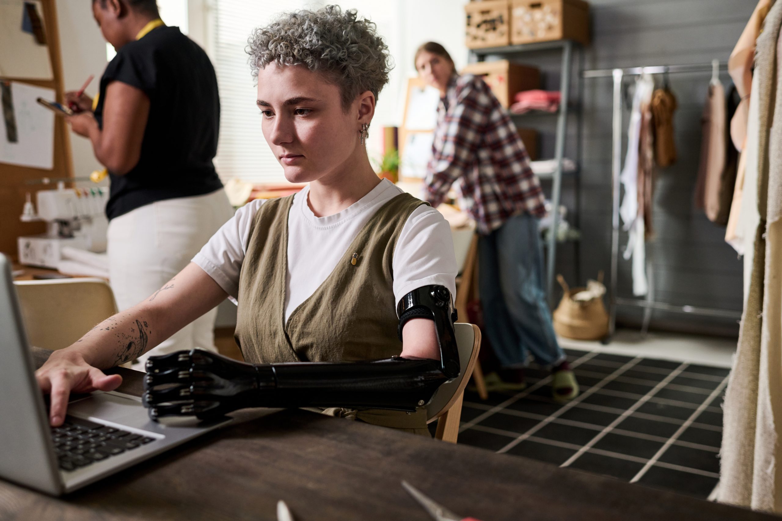 Young serious fashion designer with myoelectric arm typing on laptop keypad while looking for online information about new trends