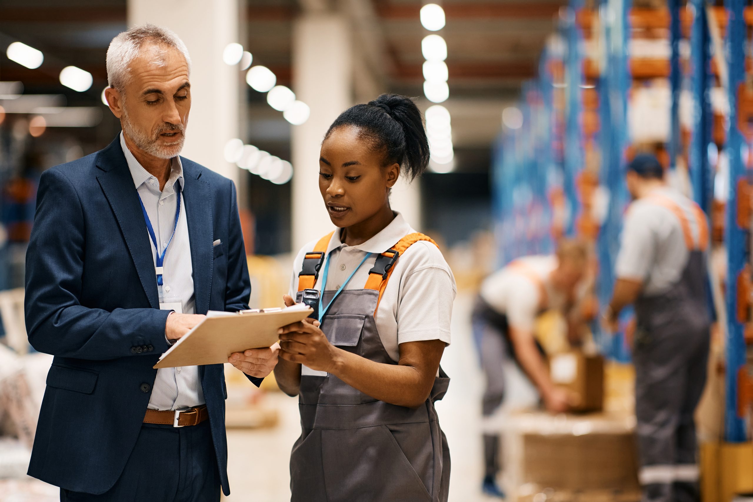 Mature manager and black female worker going through paperwork in distribution warehouse.