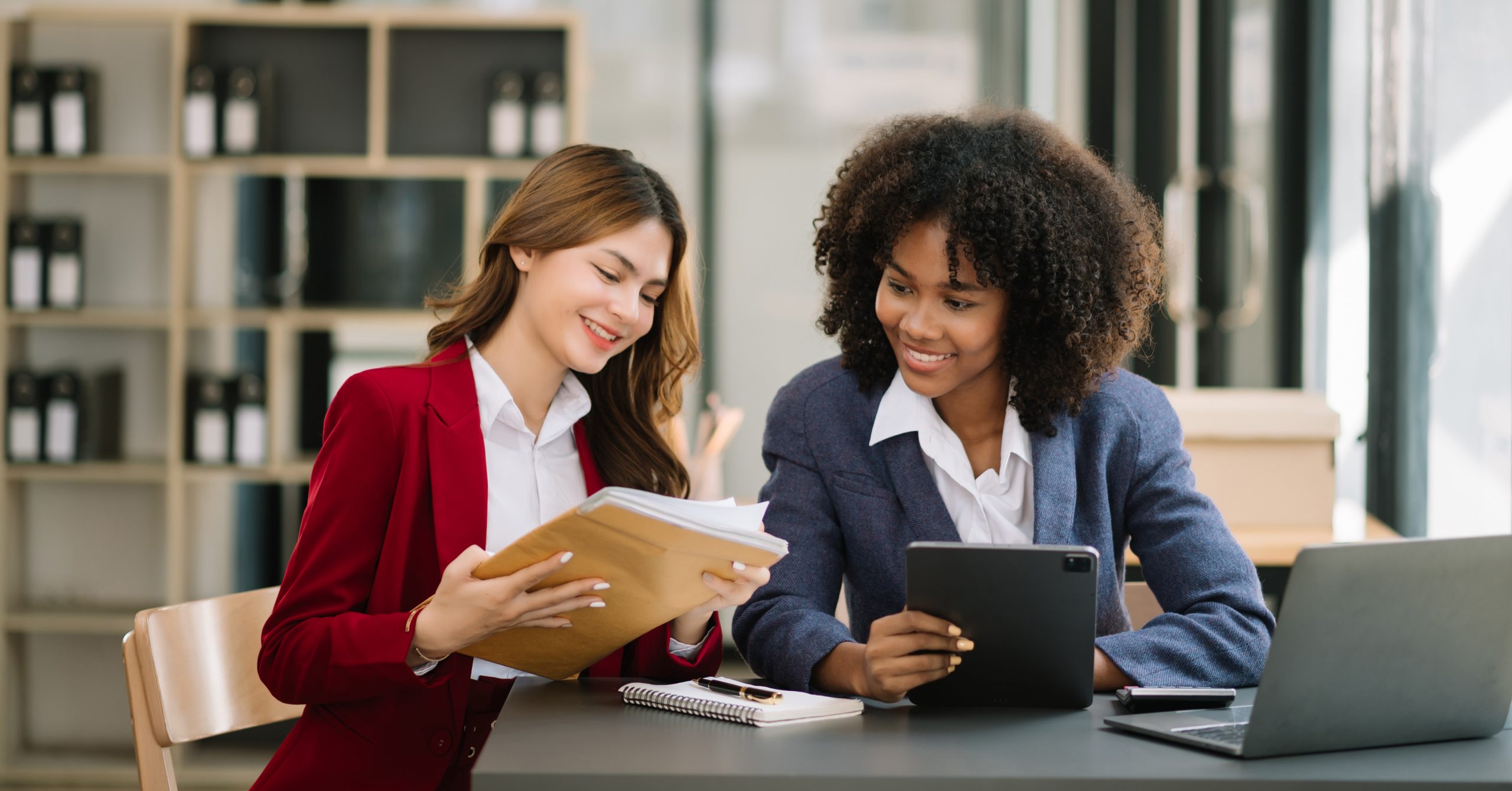 Two businesswoman discuss investment project tablet laptop computer in modern office..